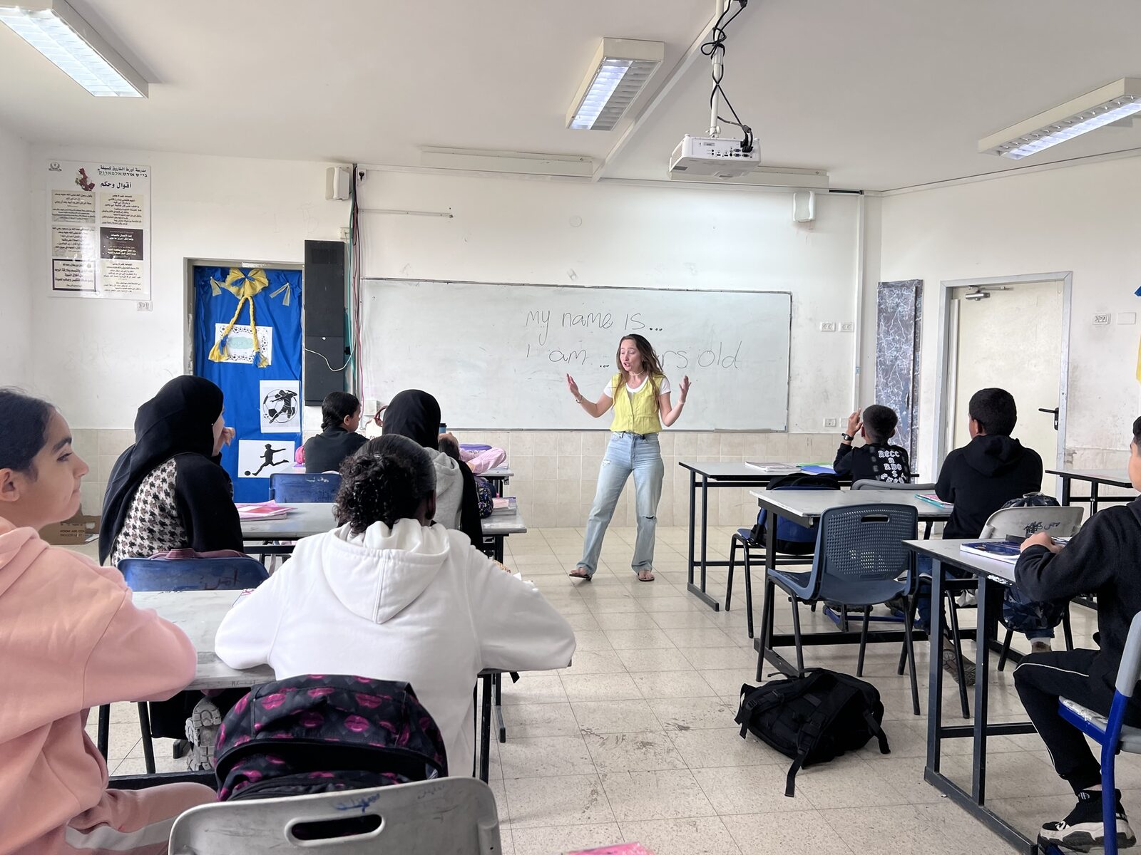 מורה מובילה שיעור אנגלית ליד הלוח בזמן שהתלמידים עוקבים